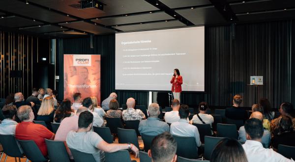 Frau steht auf Bühne und hält Vortrag.